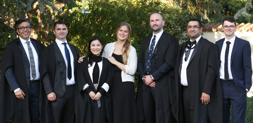 Sustainable Built Environment students Five men and two women smiling and stood in a line wearing University of Cambridge robes over formal wear.
