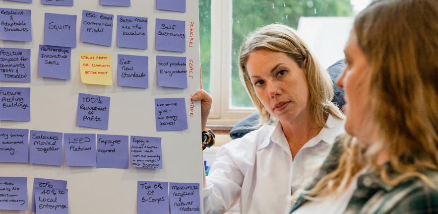 Two women presenting a board with post - it notes on it 