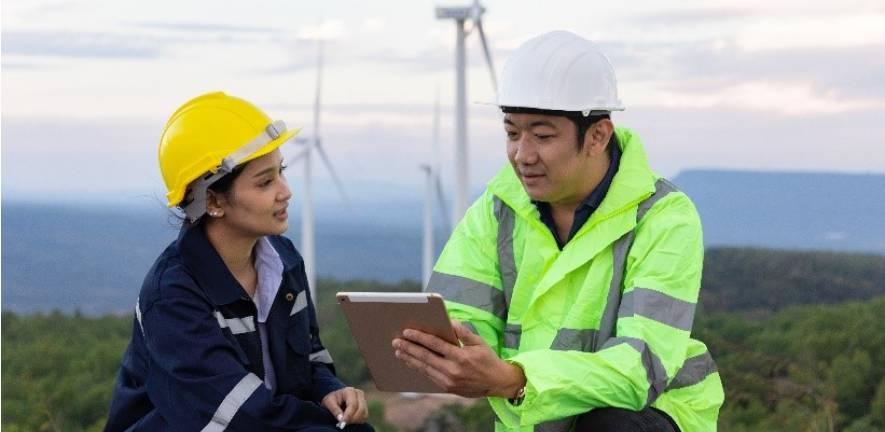 One female and one man working in a wind farm, engaged in discussion.
